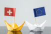 Papierschiffchen mit EU und Schweiz Flagge in Bewegung